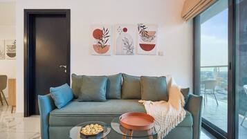 A modern living room with a green sofa, two glass tables, and artwork on the wall.