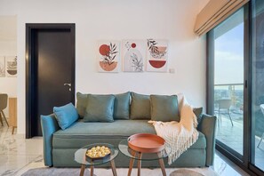 Un salon moderne avec un canapé vert, deux tables en verre et des œuvres d’art accrochées au mur.