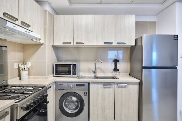 A modern kitchen with a stainless steel refrigerator, a microwave, a washing machine, and a gas stove. - Modern & Spacious 2-Bedroom Apartment in Dubai South (Dubai)