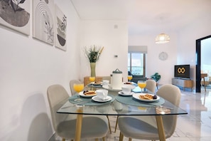 A modern dining area with a glass table, chairs, and breakfast items. - Modern & Spacious 2-Bedroom Apartment in Dubai South (Dubai)