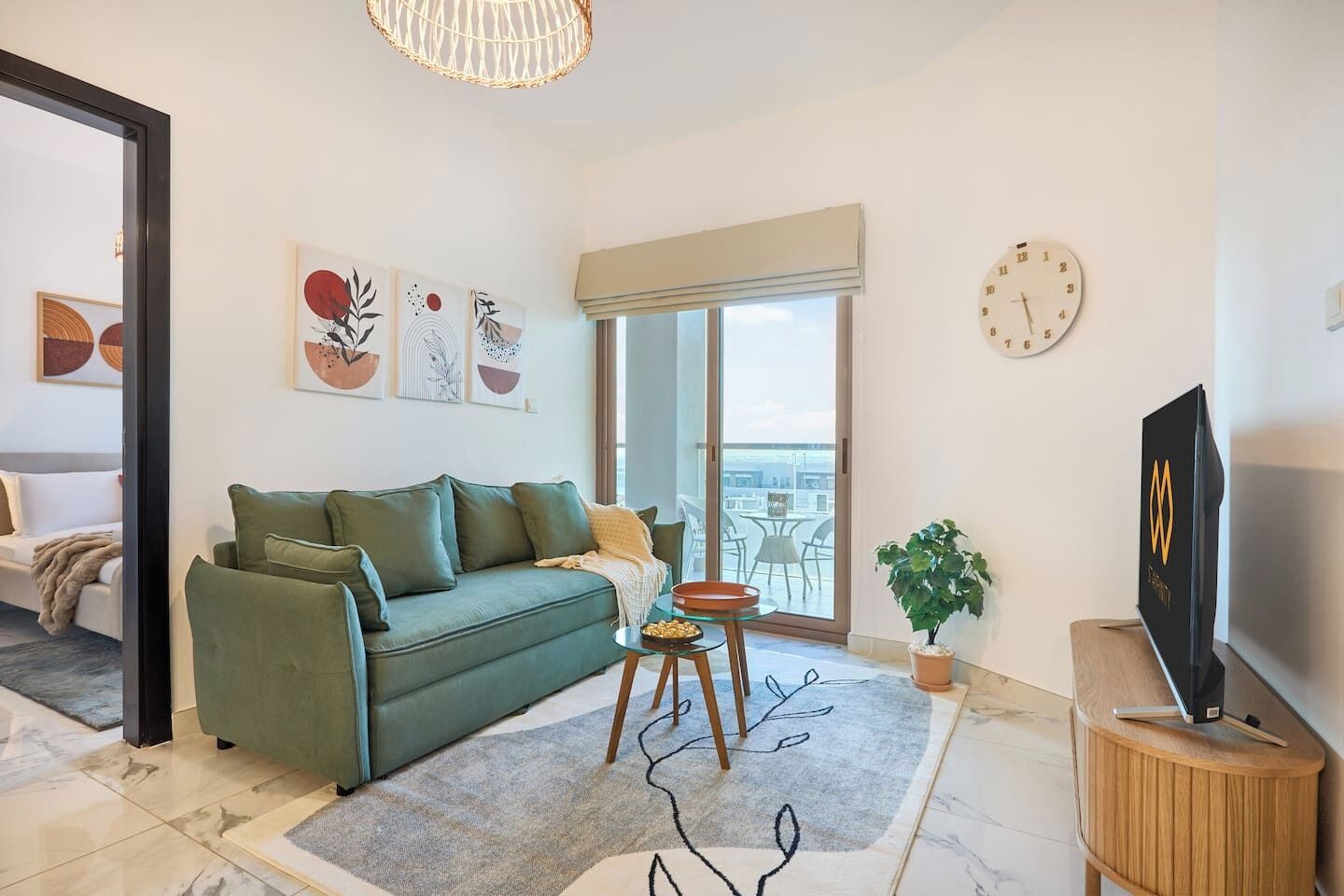 A modern living room with a green sofa, a coffee table, a TV, and a balcony with a view.