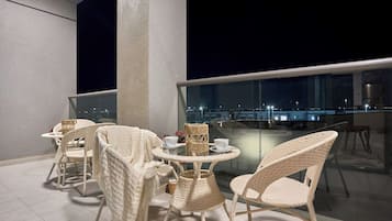 A balcony with wicker furniture, a glass table, and a view of the city at night.