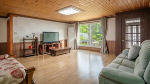 A spacious living room with a wooden ceiling, a large window with curtains, a television, and a sofa. - Ganghwado Gagopa Family Group Pension (Incheon)