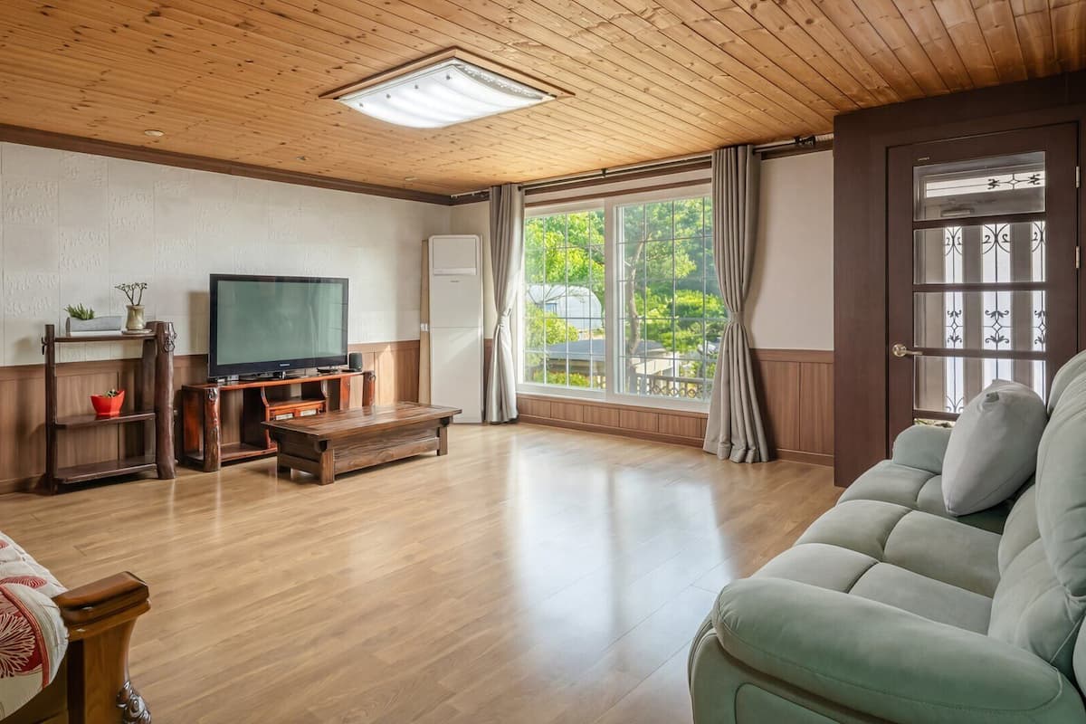 Un salón amplio con techo de madera, un ventanal con cortinas, televisor y sofá.
