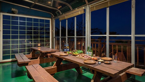 A covered outdoor dining area with a large table set for a meal, surrounded by large windows. - Ganghwado Gagopa Family Group Pension (Incheon)