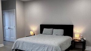 Quarto com cama, duas mesas de cabeceira com luminárias, tapete e porta.
