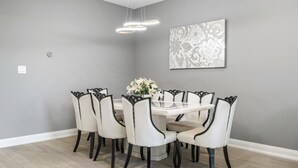 Uma sala de jantar com uma mesa redonda, seis cadeiras, um vaso de flores e uma obra de arte na parede.