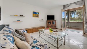 A living room with a sofa, glass coffee table, TV, wooden cabinet, and a door leading to a balcony. - House Tiziana Close by Mare Argentario, Manciano, Italy (Manciano)