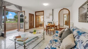 A living room with a sofa, a glass coffee table, a dining area with a table and chairs, and a view through an open door. - House Tiziana Close by Mare Argentario, Manciano, Italy (Manciano)