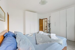 A bedroom with a bed, pillows, a blanket, and a folded towel. There is a wooden door and a white wardrobe. - House Tiziana Close by Mare Argentario, Manciano, Italy (Manciano)