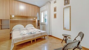 Un dormitorio con cama, armario de madera, mesita de noche, espejo y una silla.