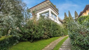 Una casa moderna con balcón de cristal, rodeada de exuberante vegetación y un sendero de piedra.