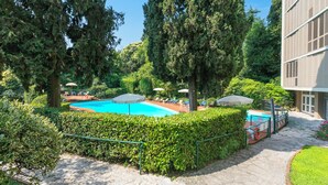 Ein Swimmingpool, umgeben von Grünflächen, ein Gebäude mit moderner Fassade und ein klarer Himmel.