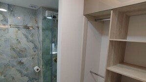 A bathroom with a glass shower enclosure, a toilet, and a wooden shelving unit. - Loft Deluxe 12th Floor Cali Velodrome View (Cali)