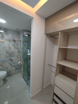 A bathroom with a glass shower enclosure, a toilet, and a wooden shelving unit. - Loft Deluxe 12th Floor Cali Velodrome View (Cali)