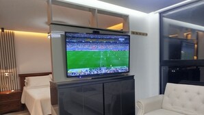 A modern living room with a flat-screen TV mounted on a cabinet, a white sofa, and a bed with a white cover. - Loft Deluxe 12th Floor Cali Velodrome View (Cali)