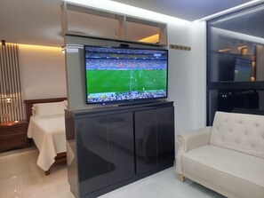 A modern living room with a flat-screen TV mounted on a cabinet, a white sofa, and a bed with a white cover. - Loft Deluxe 12th Floor Cali Velodrome View (Cali)