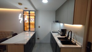 A modern kitchen with a marble countertop, a coffee maker, and a glass door with illuminated signage. - Loft Deluxe 12th Floor Cali Velodrome View (Cali)