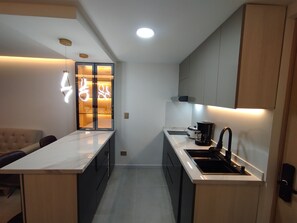 A modern kitchen with a marble countertop, a coffee maker, and a glass door with illuminated signage. - Loft Deluxe 12th Floor Cali Velodrome View (Cali)