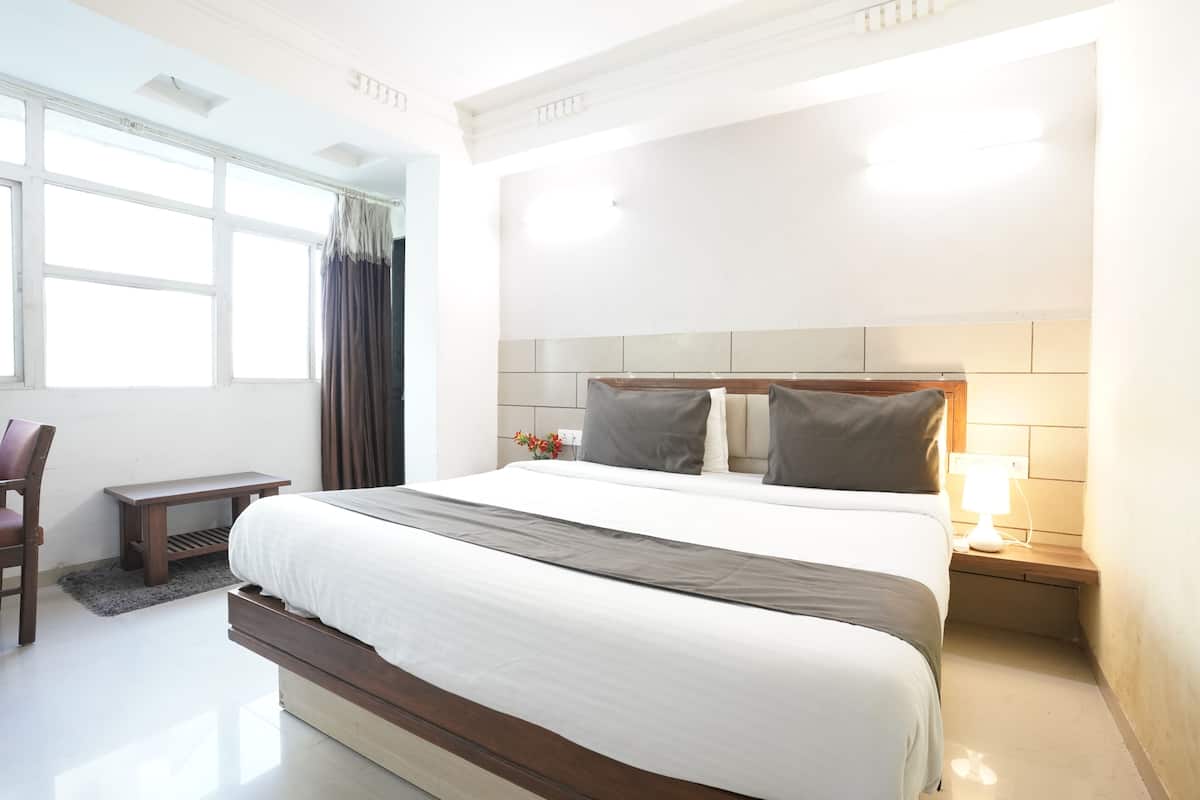 A hotel room with a large bed, a bedside table, a chair, and a window with curtains.