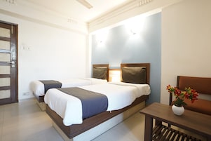 A hotel room with two beds, a wooden headboard, a small table with a vase, and a door.