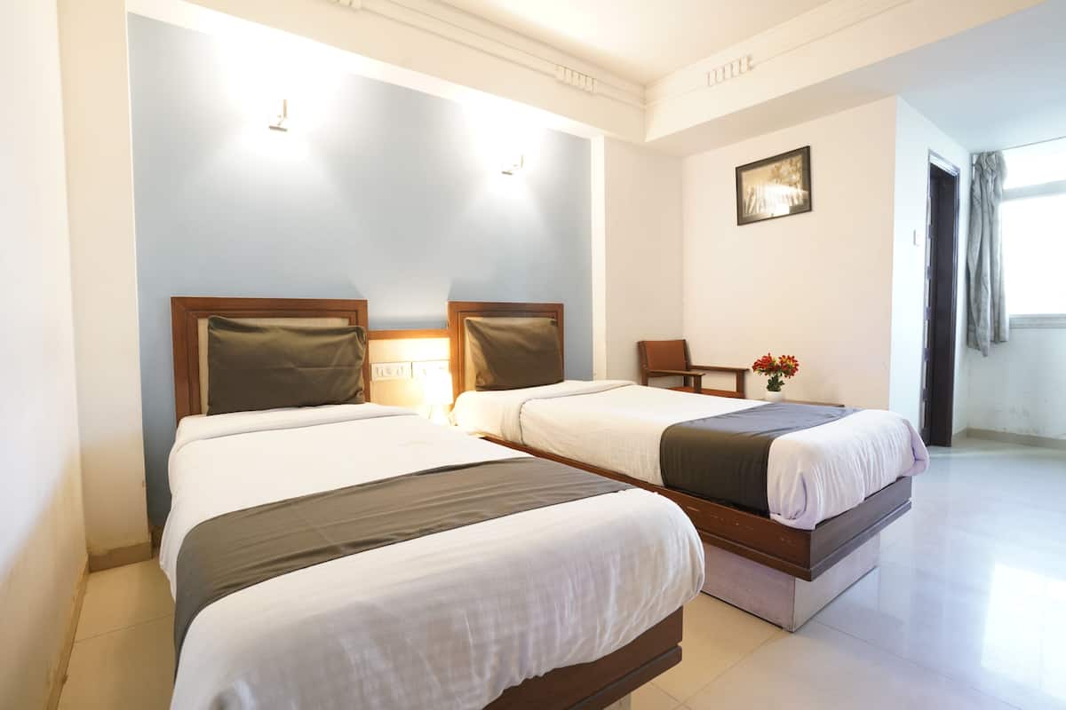 A hotel room with two beds, a chair, a small table, and a picture on the wall.