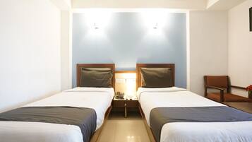 A hotel room with two beds, a nightstand, a chair, and a wall-mounted lamp.