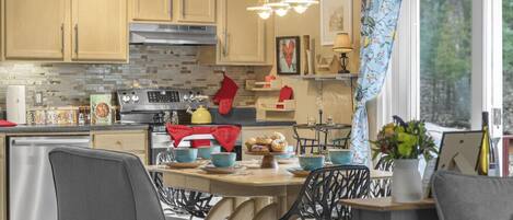 A kitchen with wooden cabinets, a stainless steel stove, and a dining area with chairs and a table.