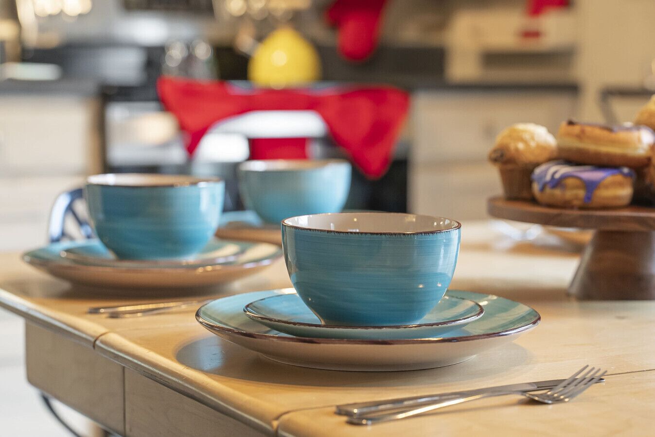 A table with blue cups and saucers, a fork, and pastries on a wooden table in a room with a red cloth in the background.