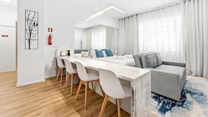 Una camera d'albergo moderna con angolo ristoro, divano e un'ampia finestra con tende.