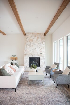 A living room with a stone fireplace, white sofa, grey armchairs, and a coffee table.