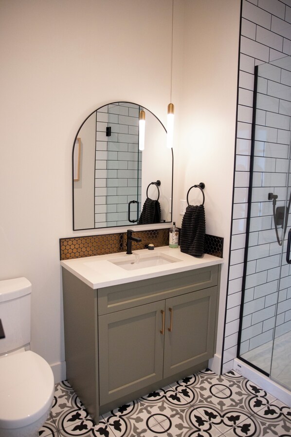 A bathroom with a toilet, sink, mirror, and shower. - Large spacious home near silver star ski resort (Vernon)