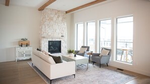 A living room with a stone fireplace, a sofa, a coffee table, and a view through large windows. - Poolside retreat with private basketball court (Vernon)