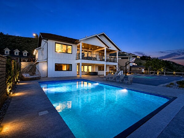A two-story house with a swimming pool, outdoor seating, and a view of the surrounding landscape.