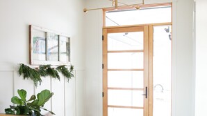 A hallway with a wooden door, a plant, a bench, a hanging light fixture, and a window with blinds. - Poolside retreat with private basketball court (Vernon)