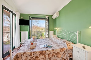 Ein Schlafzimmer mit Bett, Nachttisch, Fernseher und Balkonblick.