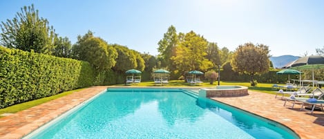 A rectangular swimming pool with a tiled deck, surrounded by a well-maintained hedge and trees.
