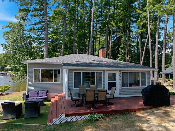 A cabin with a deck, outdoor seating, and a view of a lake.