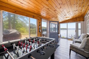 A wooden-floored room with a foosball table, large windows, and a view of a lake.