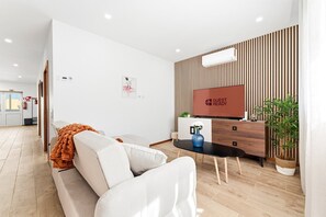 A modern hotel room with a sofa, a small table, a TV, and a wooden panel wall.