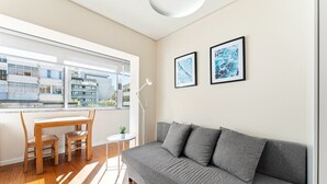 Una sala moderna con un sofá gris, una mesa de comedor de madera, sillas, una mesita auxiliar con una lámpara y dos obras de arte enmarcadas en la pared.