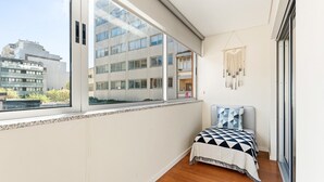 Un dormitorio con un ventanal grande, una cama con ropa de cama estampada y un tapiz de macramé en la pared.
