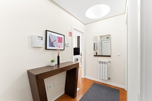Ein Hotel-Empfangsbereich mit einem Holztisch, einer gerahmten Karte, einem kleinen Topfpflanzen, einem Spiegel, einem Thermostat und einem Heizkörper.