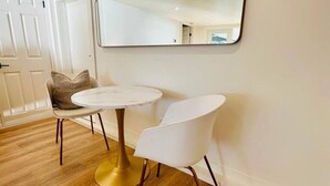 A dining area with two white round tables, a gold pedestal base, and a large mirror on the wall. - Gorgeous Ocean & Mountain View King Suite (Bowen Island)