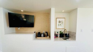 A modern kitchen with a flat-screen TV, wooden shelves, and a framed picture. - Gorgeous Ocean & Mountain View King Suite (Bowen Island)