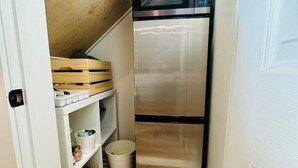 A narrow hallway with a stainless steel refrigerator, wooden storage boxes, and a white trash bin. - Gorgeous Ocean & Mountain View King Suite (Bowen Island)