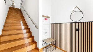 A wooden staircase with a metal handrail, a wall-mounted circular object, and a black metal rack with a shelf. - GuestReady - Apartment near beach retreat (Vila do Conde)