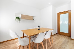 A dining area with a wooden table, white chairs, a small plant, and a door with frosted glass.