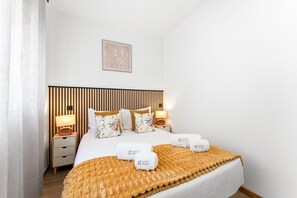 A hotel room with a bed, bedside tables, a headboard, a wall-mounted artwork, and a bedspread.