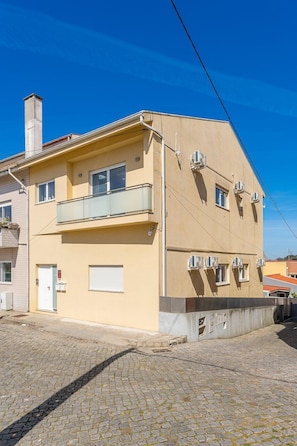 A two-story building with a balcony, air conditioning units, and a chimney.